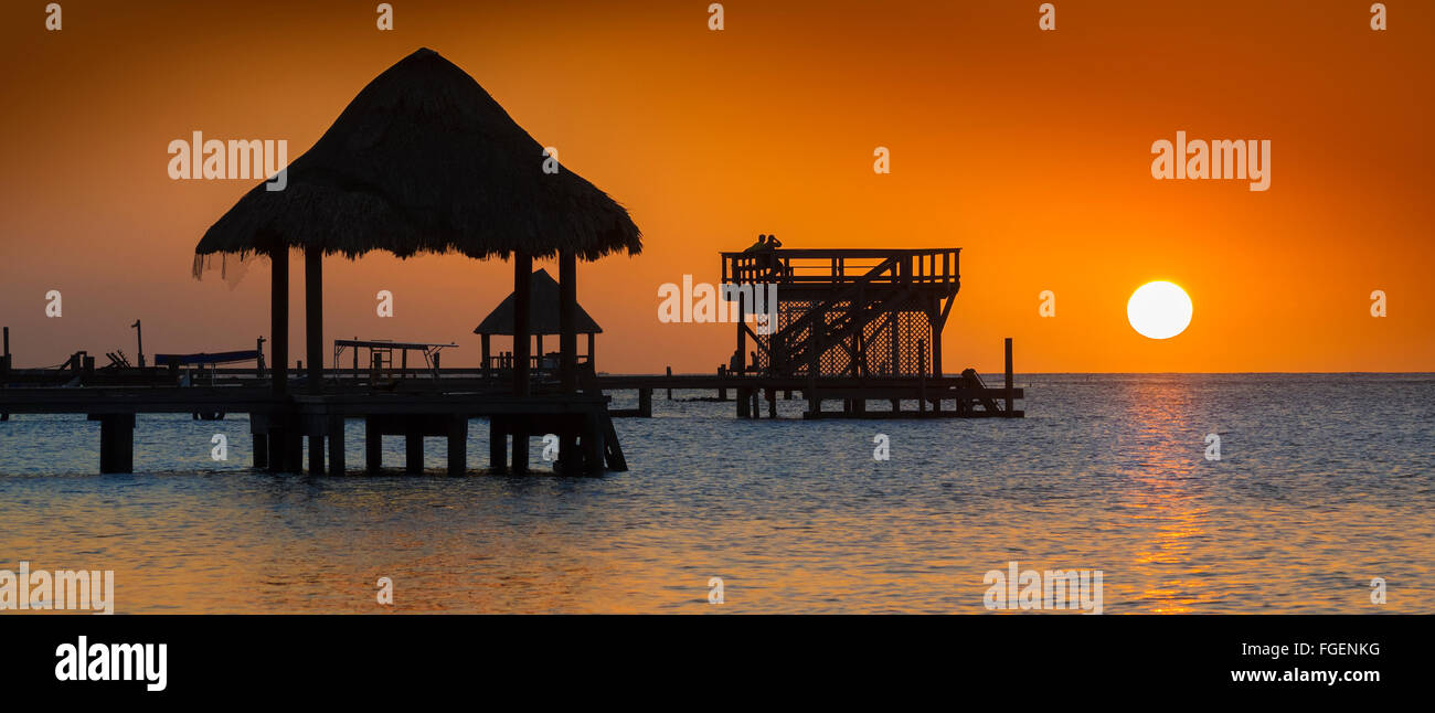 Bungalow en la playa iluminada desde atrás por un atardecer naranja en Roatán, Honduras Foto de stock