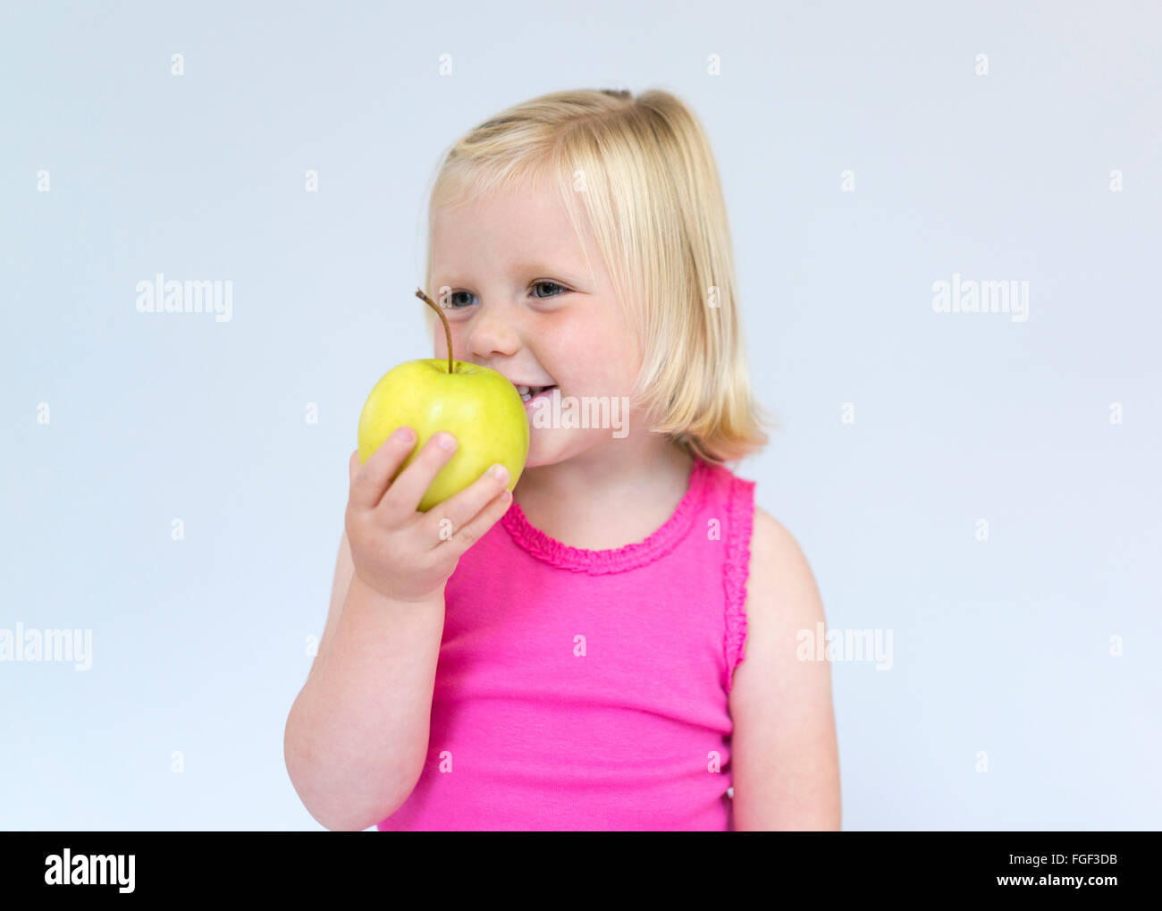 Muchacha con cabello rubio sosteniendo una manzana verde sonriendo Foto de stock