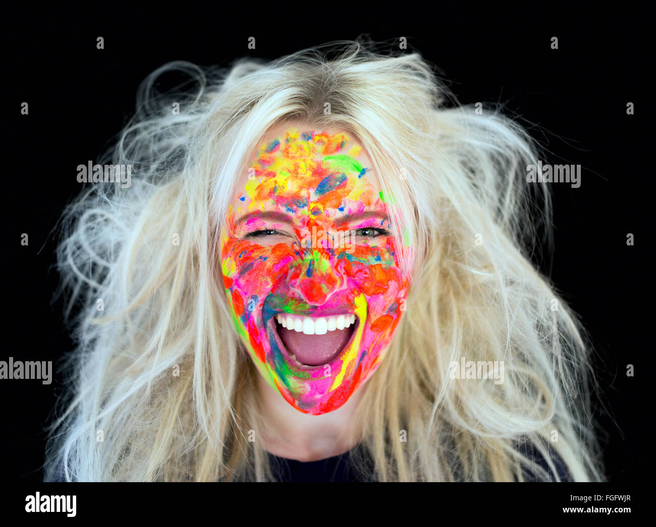Mujer con cabello rubio desordenado con el rostro cubierto de pintura multicolor riendo Foto de stock
