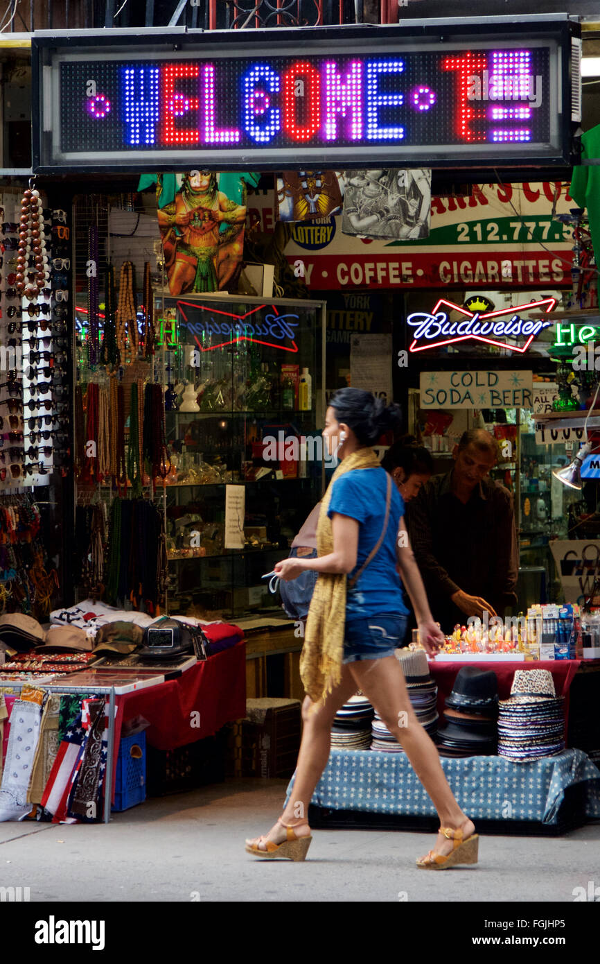 Mujer joven camina por una típica calle de San Marcos tienda como una sobrecarga cartel de neón que dice "bienvenidos" en el East Village, New York, NY. Foto de stock