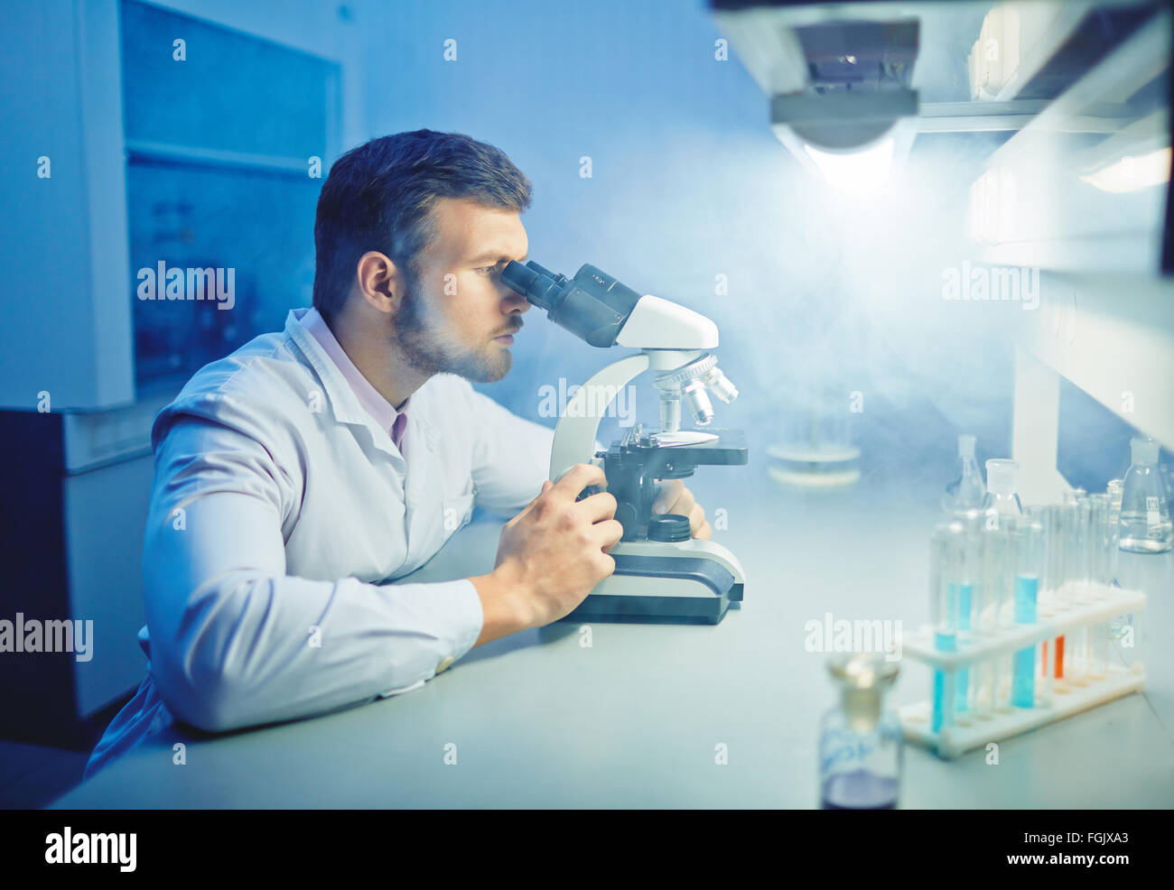 El científico contemporáneo con microscopio llevando a cabo investigación microbiológica Foto de stock