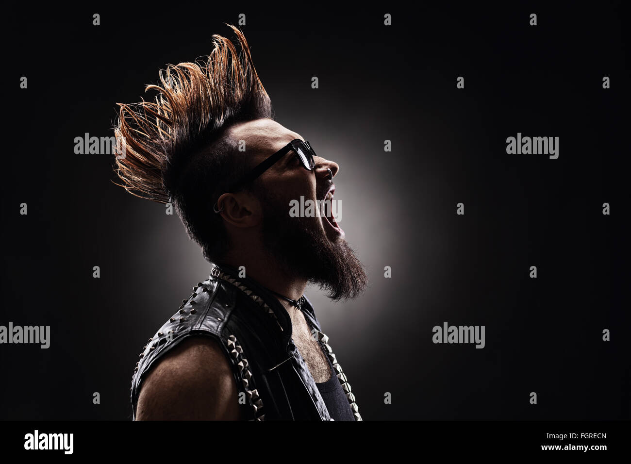 Foto de perfil de un rockero punk furiosa gritando sobre fondo oscuro Foto de stock