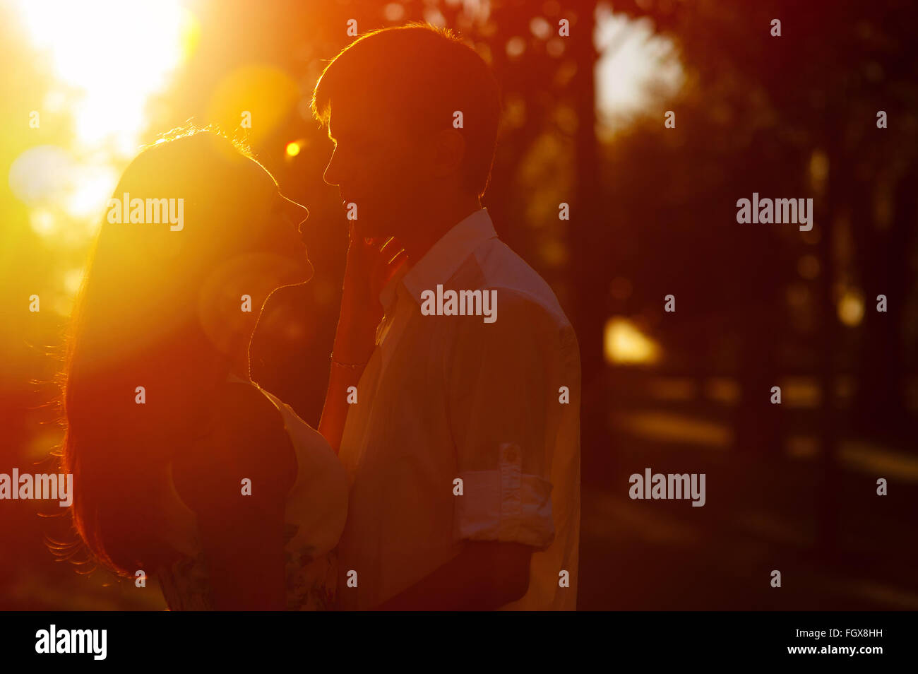 Pareja joven silueta abrazando y mirando a uno y otro al aire libre en el sunset Foto de stock