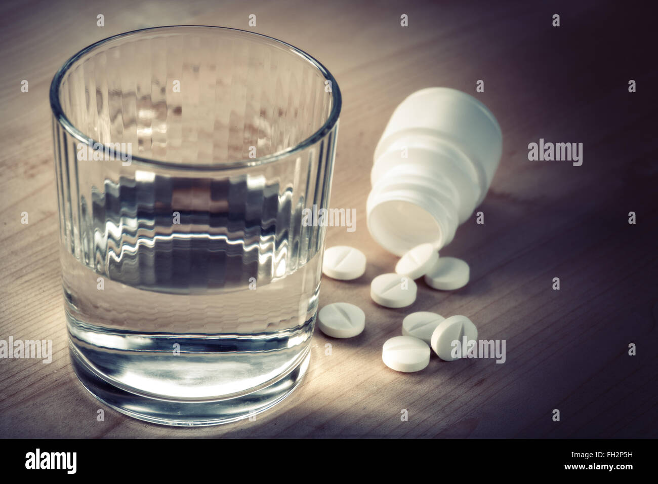 Analgésico. Resumen Antecedentes médicos con píldoras y un vaso de agua encima de un mostrador de madera Foto de stock