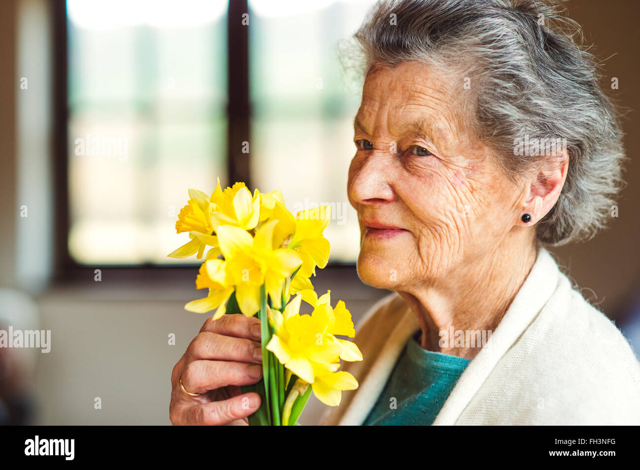 Mujer mayor por la ventana sosteniendo ramo de narcisos Foto de stock