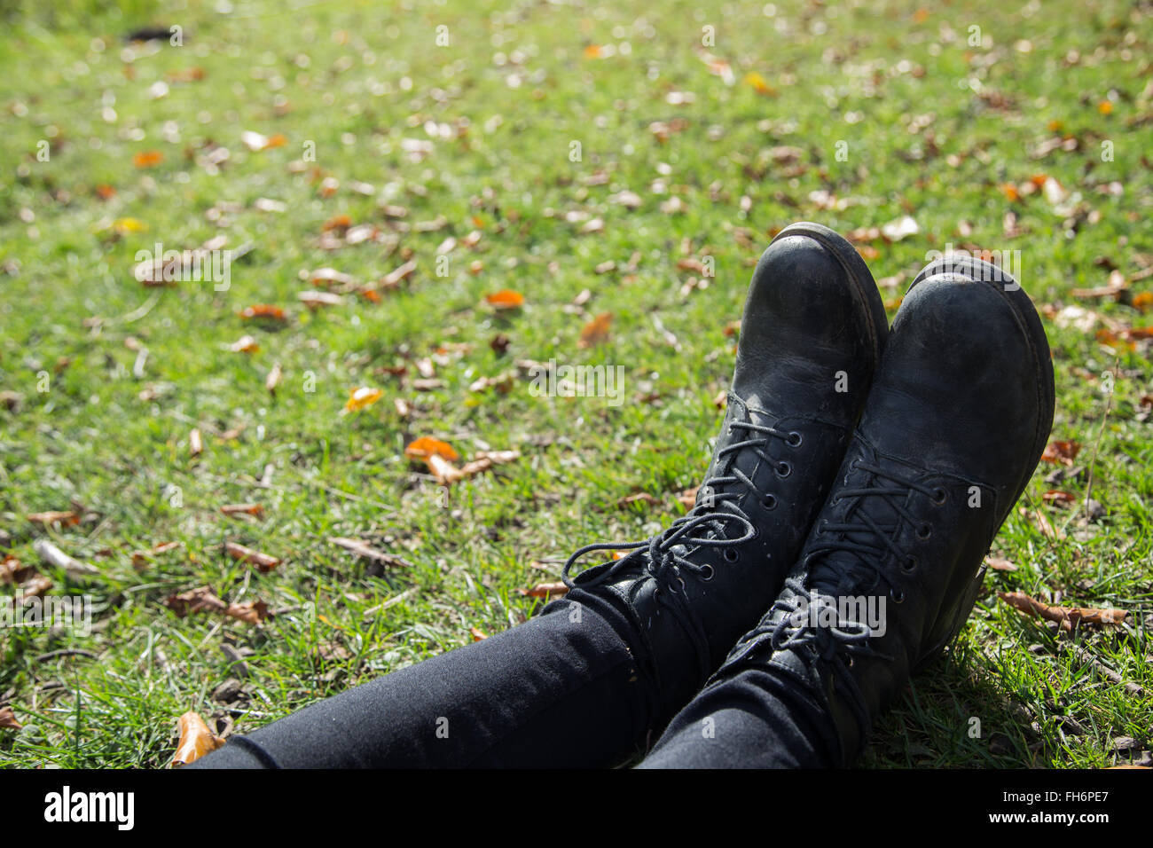 Una fotografía de una niña botas y pantalones negros en la hierba. Foto de stock