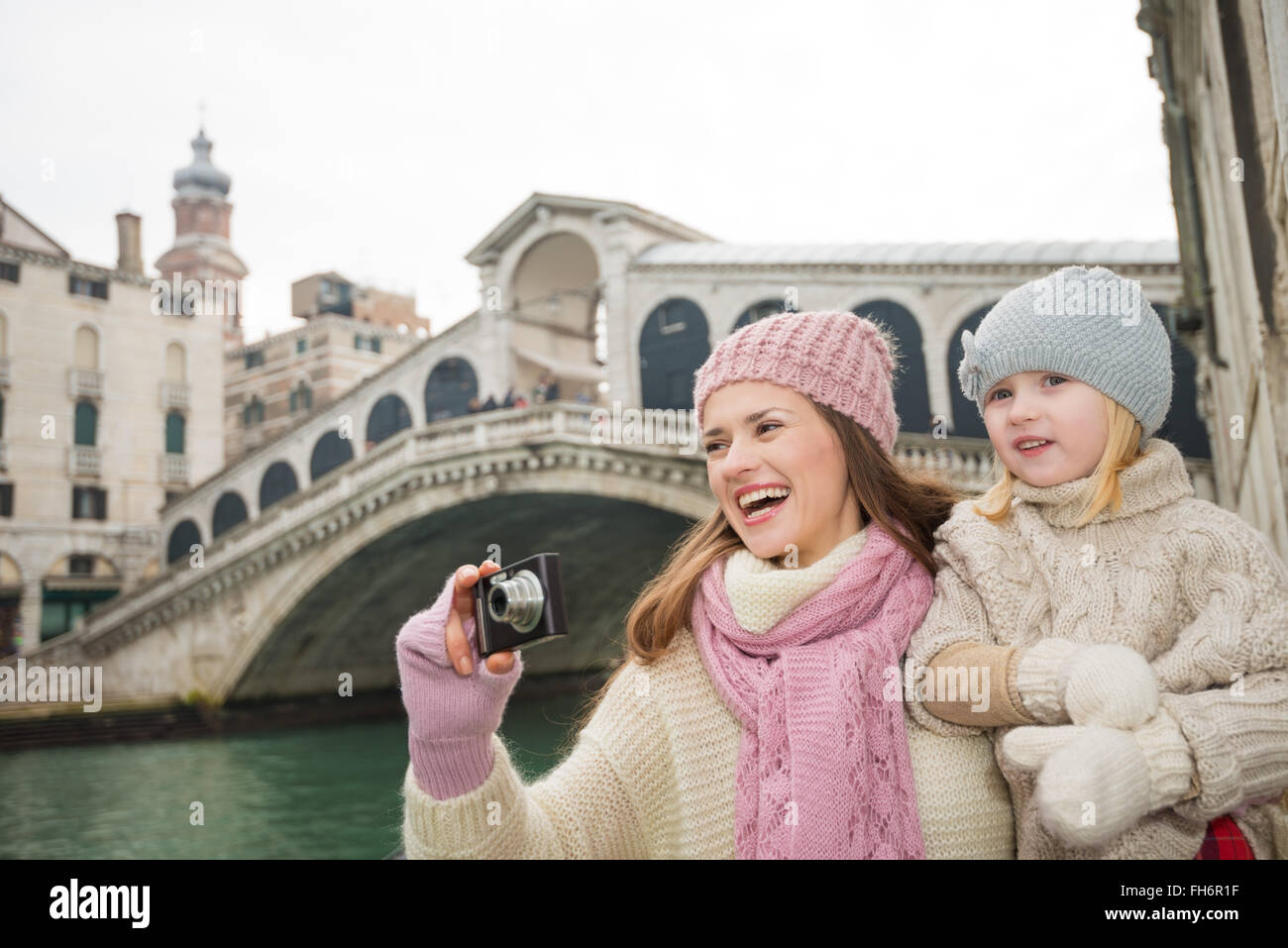 Familia moderna teniendo un receso de invierno para disfrutar de la aventura inspiradora en Venecia, Italia. Madre e hija feliz tomando fotos mientras está de pie delante del puente de Rialto Foto de stock