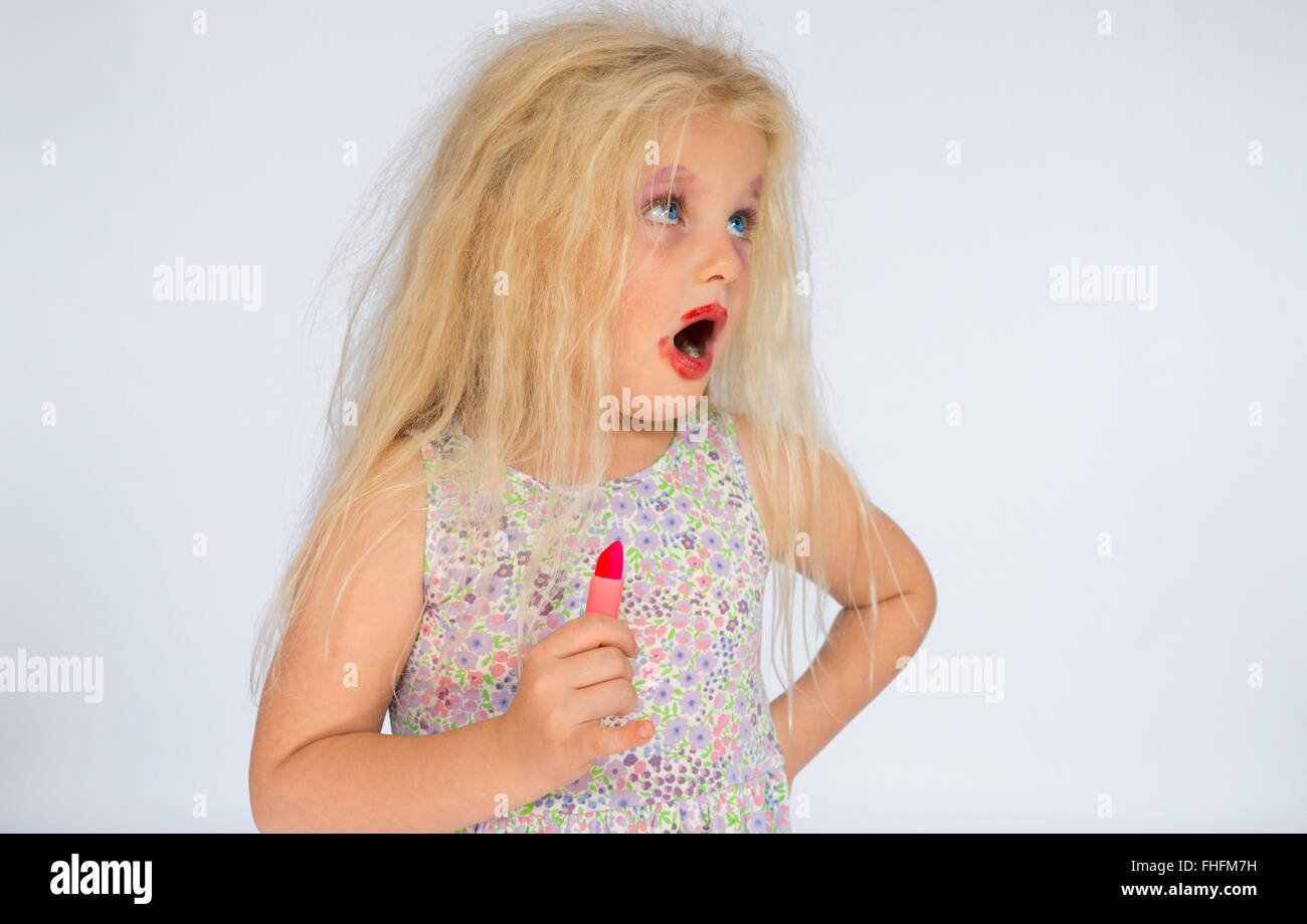 Joven sosteniendo un lápiz labial rojo con largo pelo rubio desordenado vistiendo manchado de pintalabios rojo Foto de stock