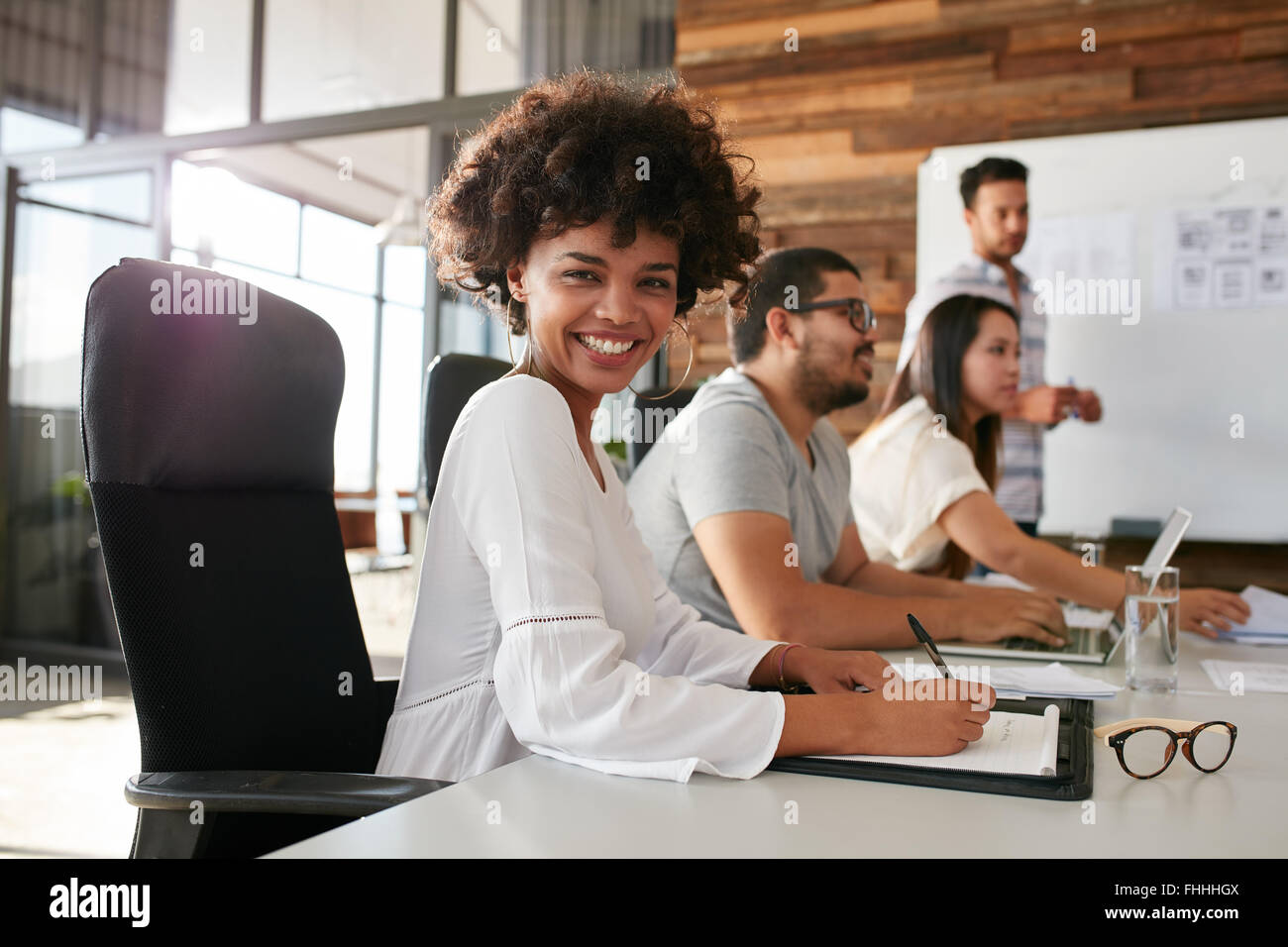 Retrato de feliz joven africana sentado en la presentación de un negocio con sus colegas en la sala de juntas. Diseñador con cowo femenino Foto de stock