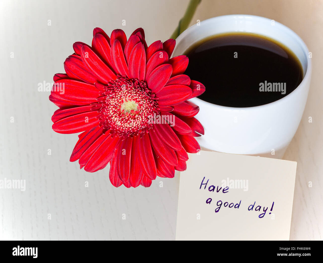 Gerbera Roja flor, una taza de café y un papel con el texto ''tenga un buen día!" en el mostrador de madera. El enfoque selectivo, tonificada Foto de stock