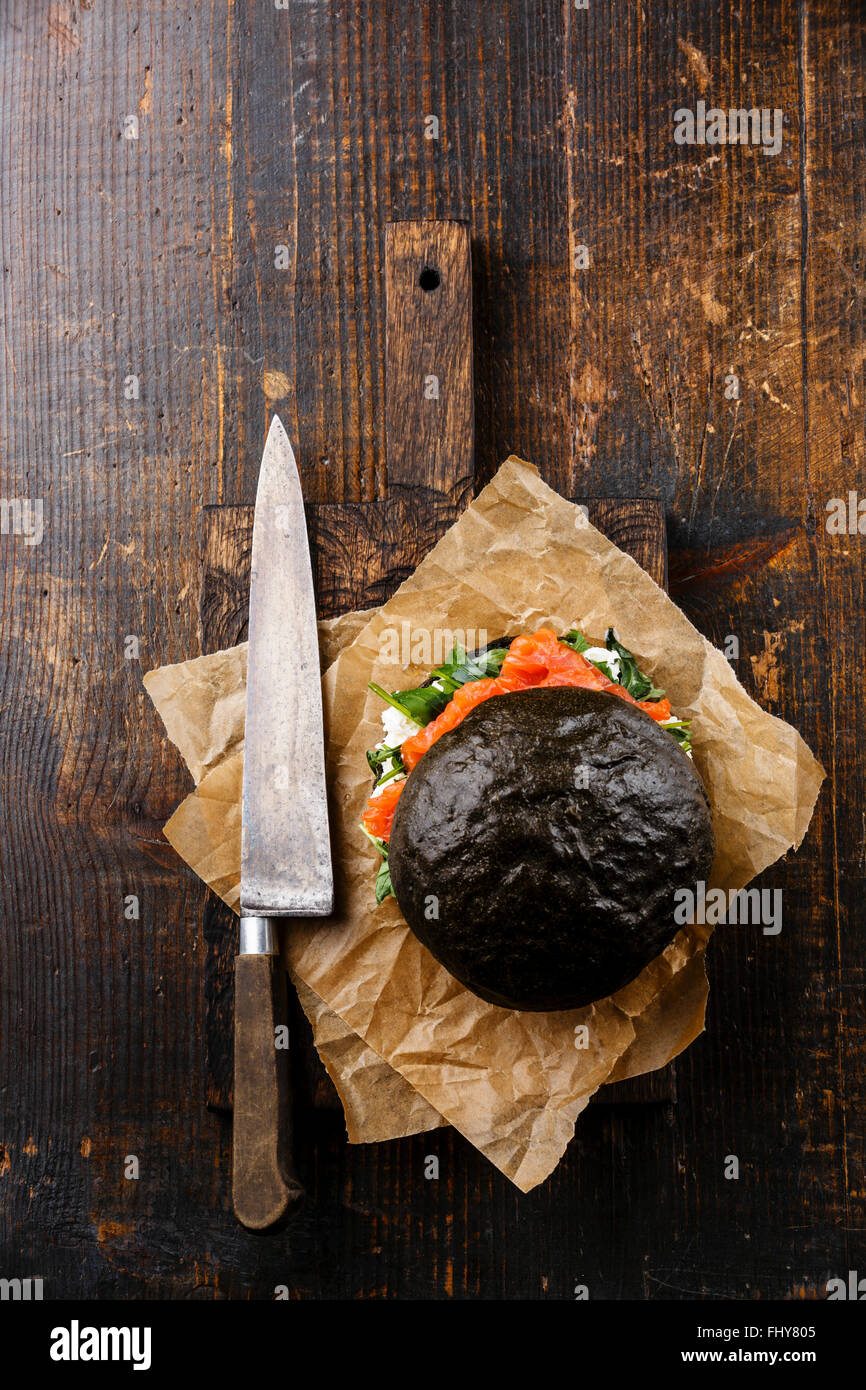 Negro hamburguesa de salmón con crema de queso y rúcula sobre placa de corte sobre fondo de madera oscura. Foto de stock