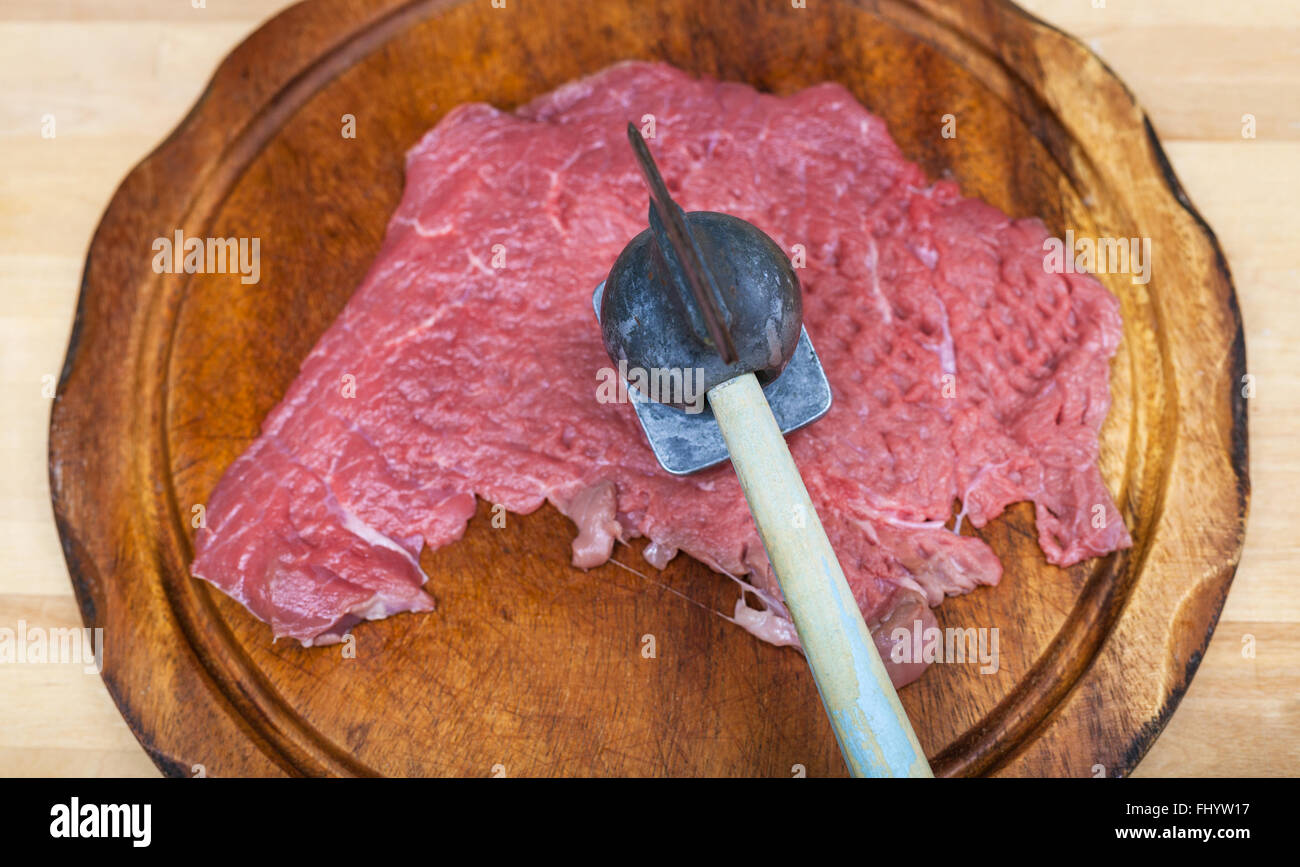 Vista superior del trozo de carne de ternera cruda está latiendo por el ablandador de carne en la placa de corte Foto de stock