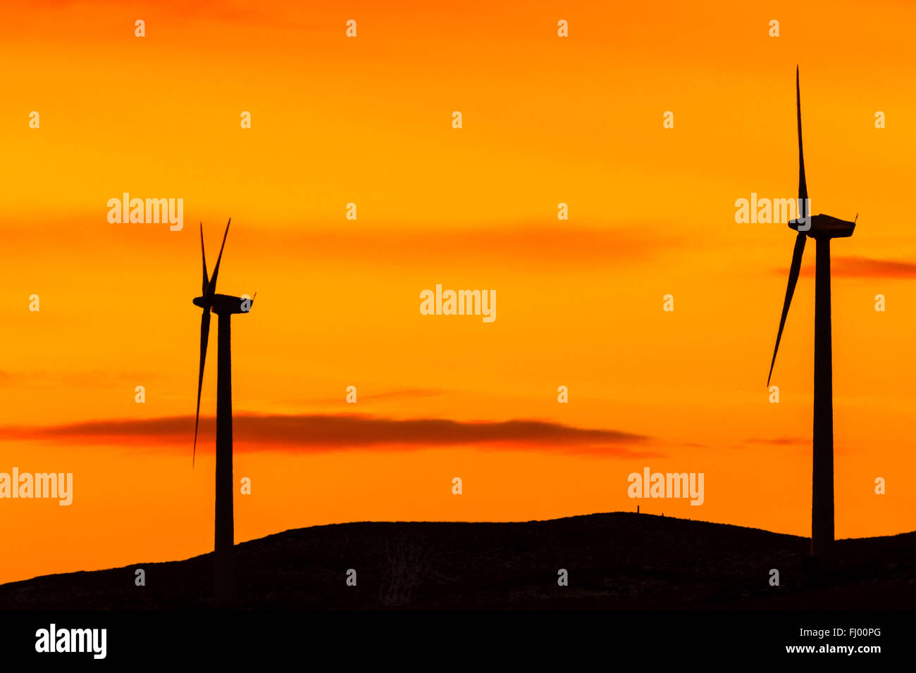 Silueta de dos aerogeneradores contra un cielo naranja Foto de stock