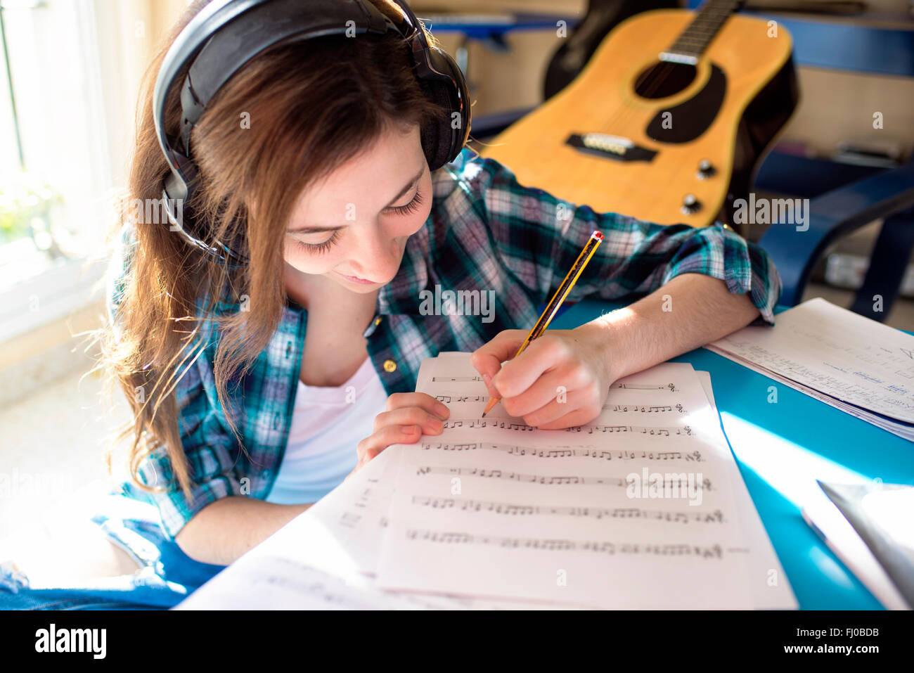Mujer joven usando audífonos escrito sobre partituras Foto de stock