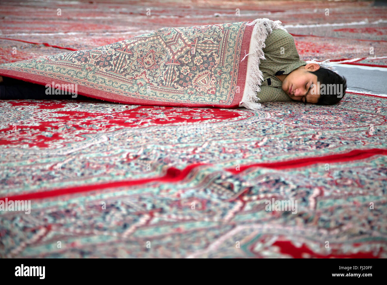 Hombre dormido envuelto en una alfombra en Irán en el mausoleo del ayatolá Jomeini, Teherán , Irán Foto de stock
