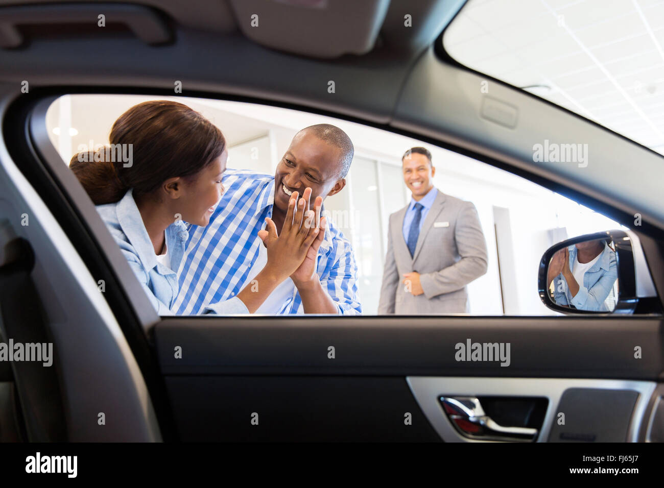 Emocionada pareja africana en el concesionario comprando coche nuevo Foto de stock
