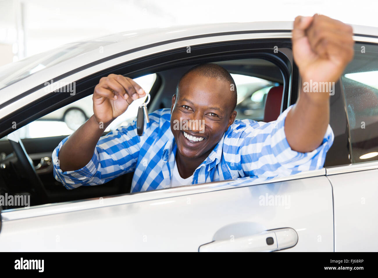 Emocionado hombre africano mostrando una llave del coche en el interior de su vehículo nuevo Foto de stock