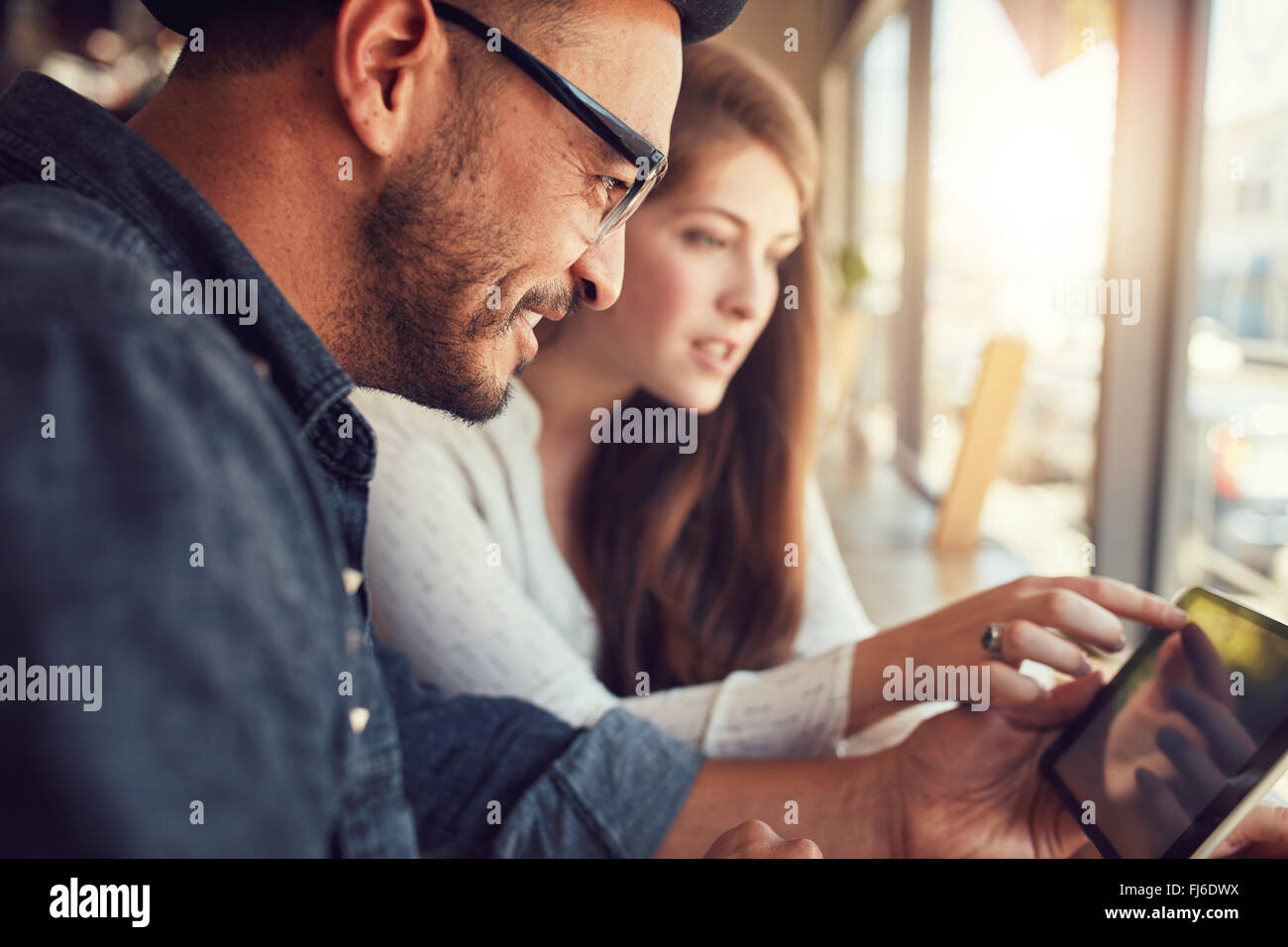 Feliz joven con su novia en una cafetería navegando por internet en tableta digital. Pareja joven en un restaurante mirando Foto de stock