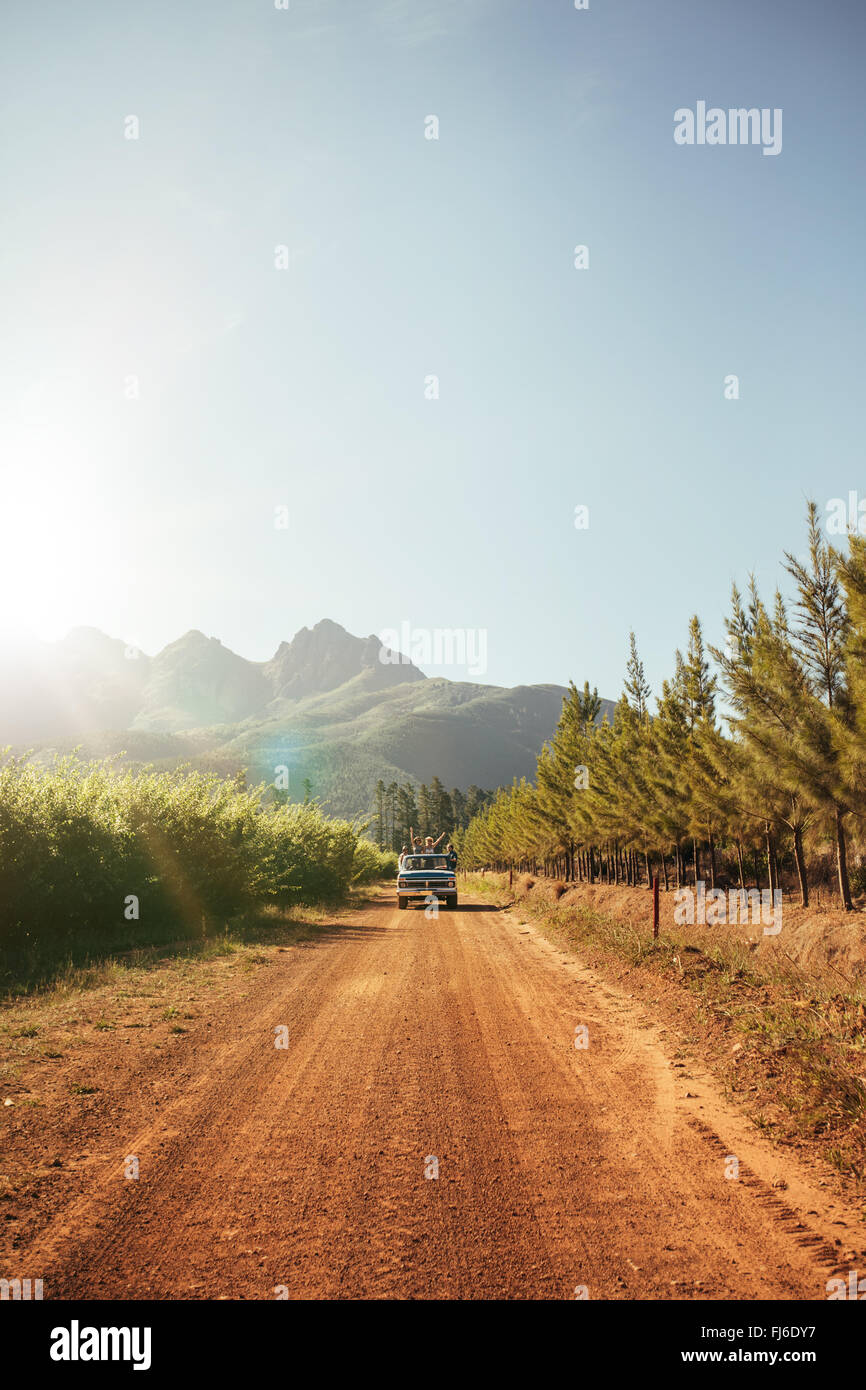 La imagen exterior del coche distante llegando en un camino de tierra rural en un día soleado. Conducción de automóviles a través del país por carretera. Foto de stock