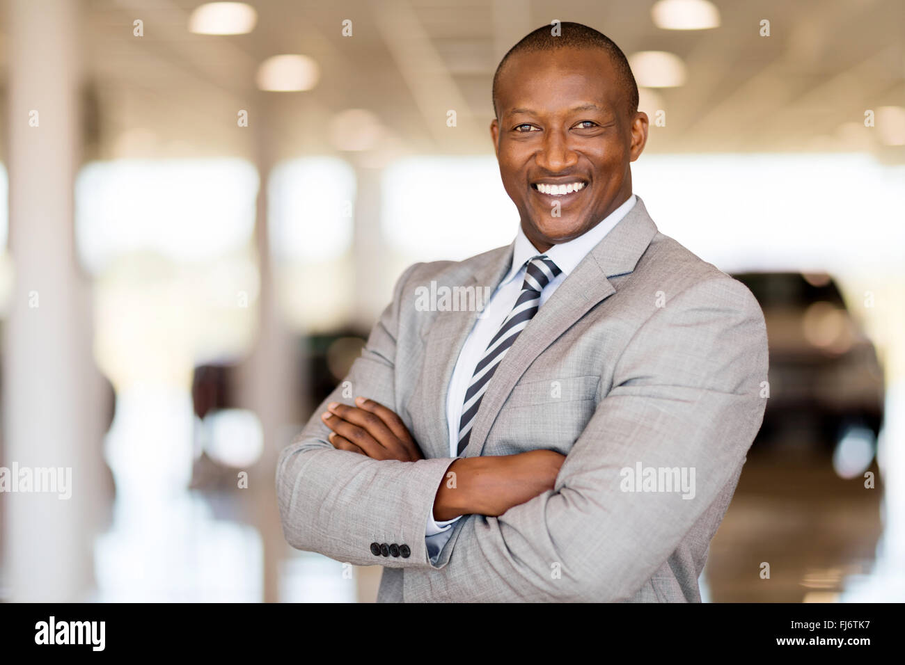 Consultor de ventas de automóviles africano con los brazos plegados en showroom Foto de stock