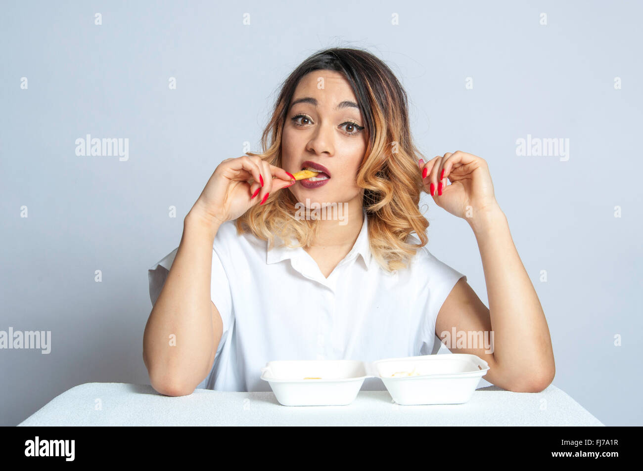 Británico joven muchacha asiática comiendo fichas en ajuste studio, London, England, Reino Unido Foto de stock