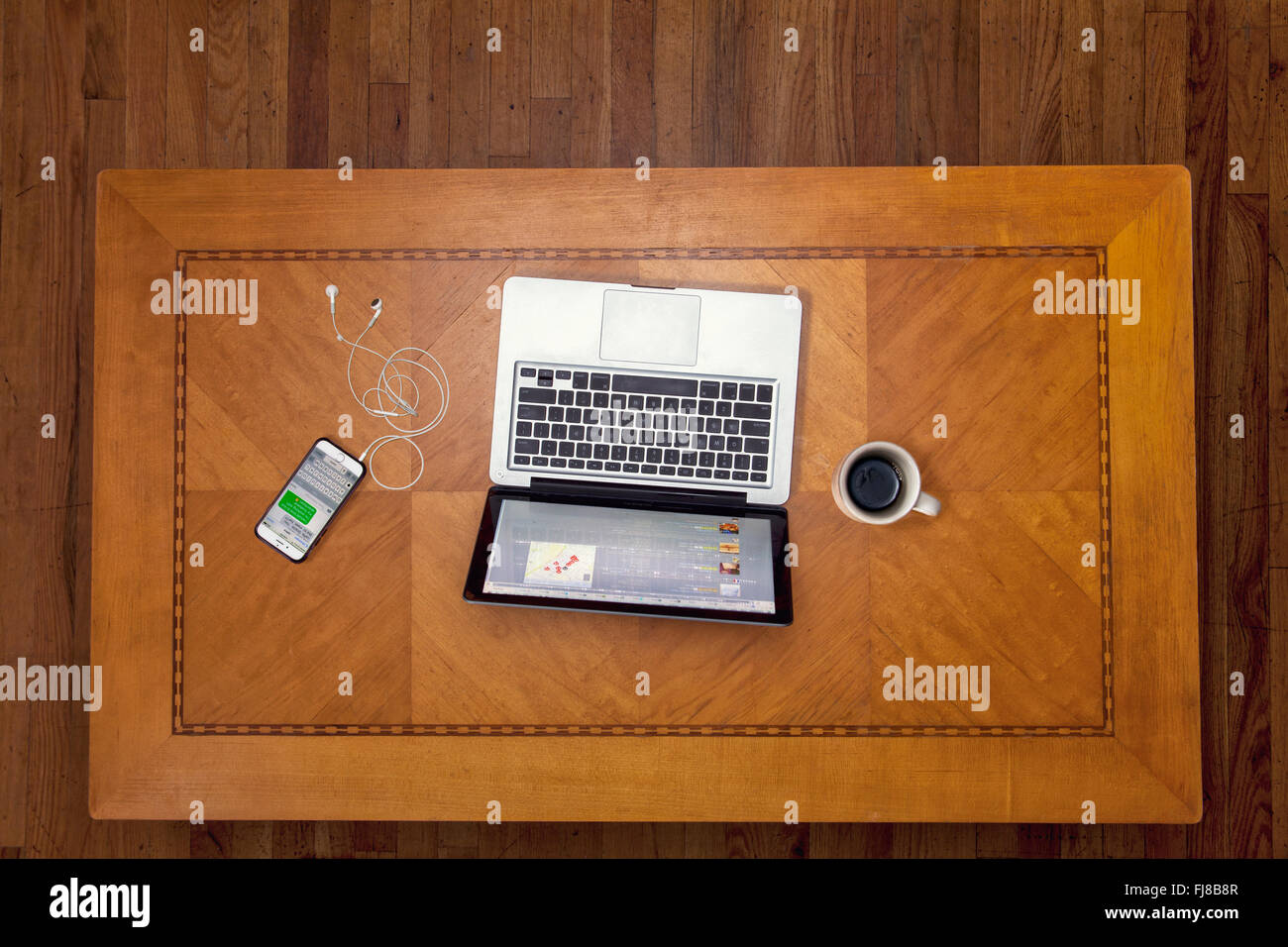 Mirando hacia abajo sobre una mesa art deco con un ordenador portátil, iphone y la taza de café. Foto de stock