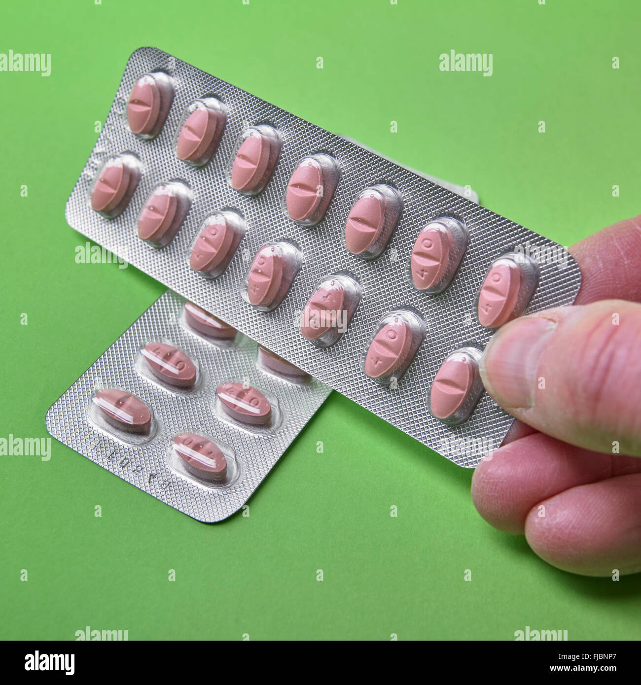 Hombre mano sujetando las estatinas, medicamentos que reducen el colesterol, en envases tipo blister sobre fondo verde Foto de stock