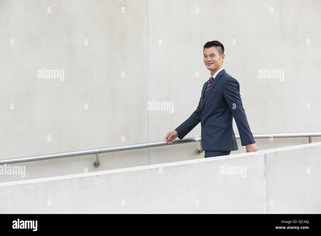Vista lateral de un empresario asiático feliz caminando por las calles de la ciudad. Foto de stock