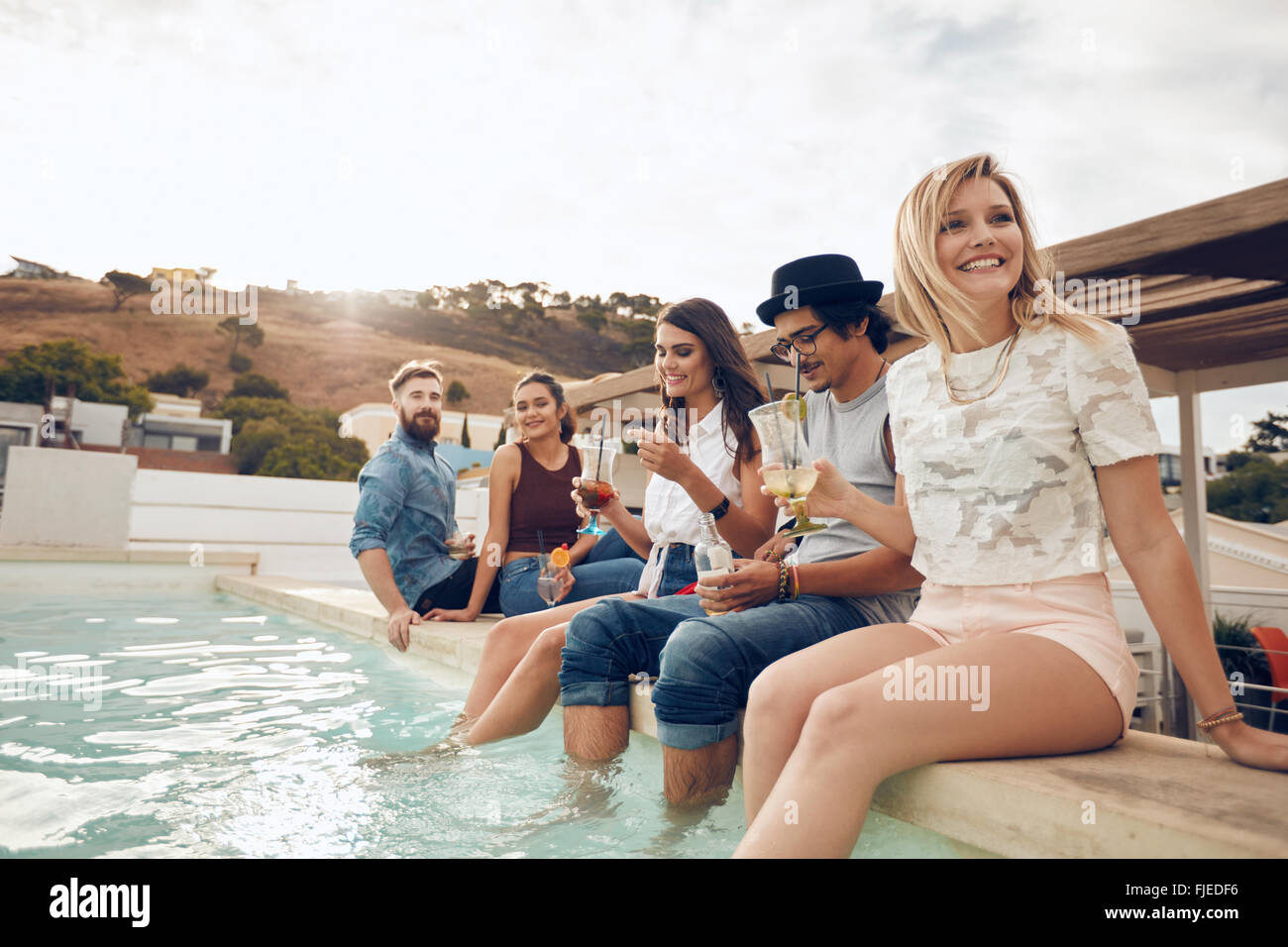 Grupo multiétnico de jóvenes paseándose por la piscina la celebración de cócteles. Feliz amigos disfrutando de fiesta en la piscina. Foto de stock