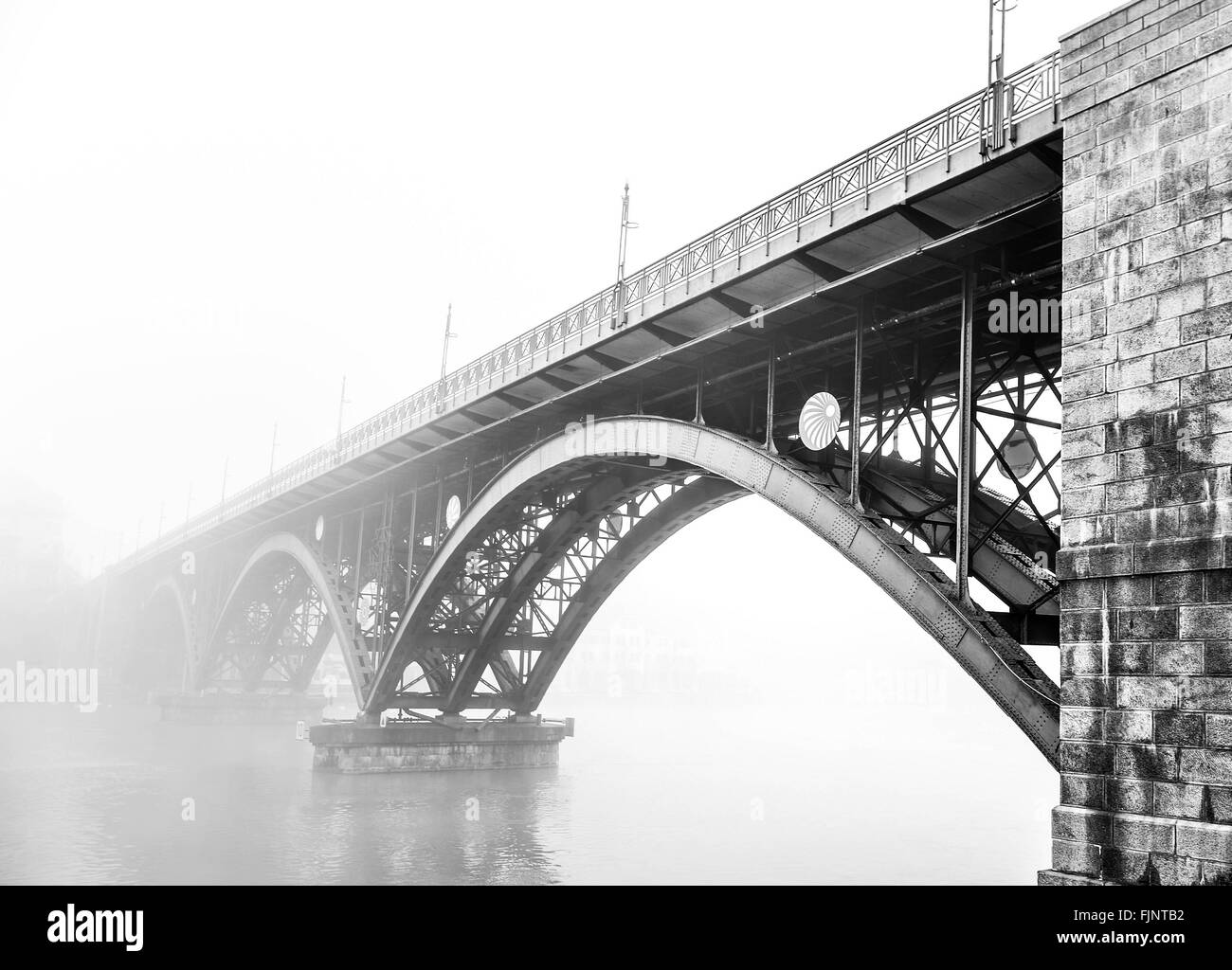Puente en arco sobre el lago en calma en la Niebla contra el cielo claro Foto de stock