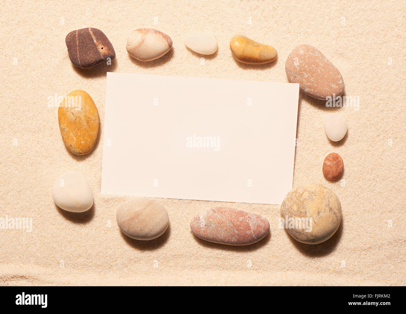 Bastidor rectangular de piedras marinas con tarjeta de visita blanco sobre la arena. Fondo de verano en la playa. Vista desde arriba Foto de stock