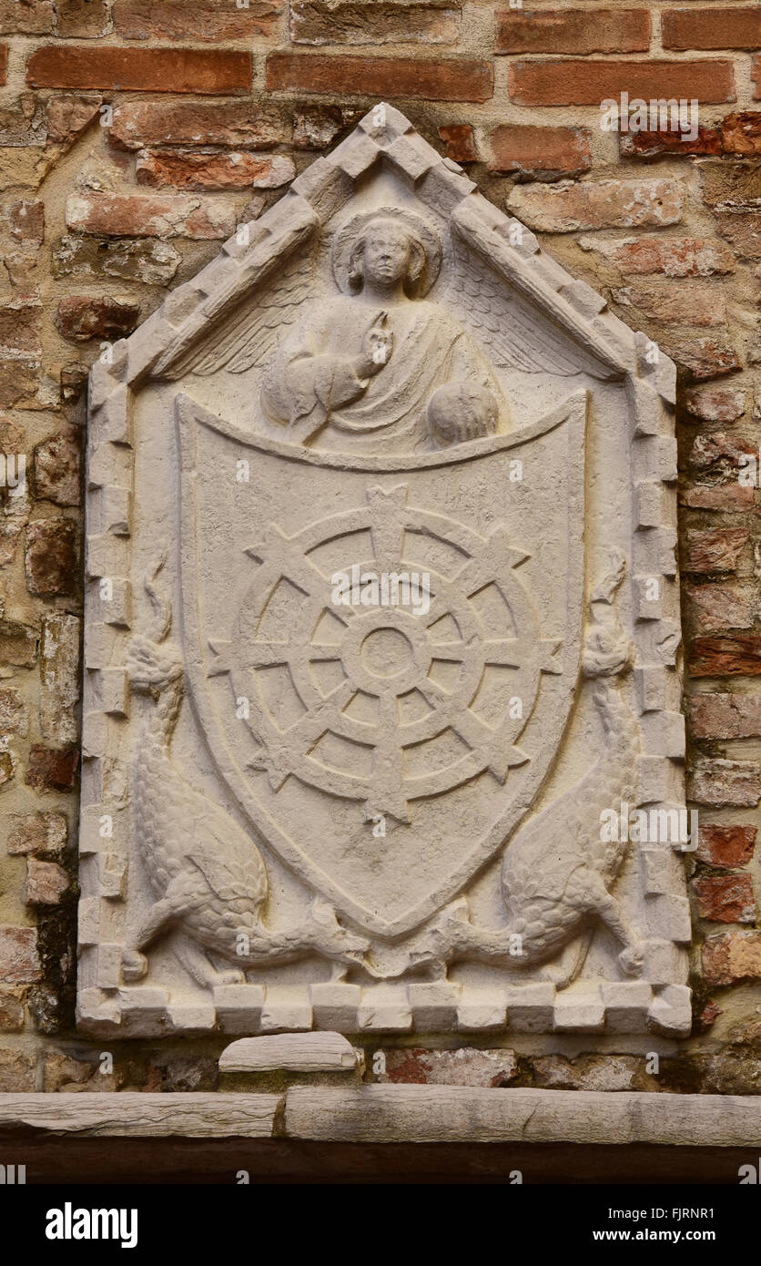 Medieval típico veneciano (plaza formella alivio en una pared) de un escudo con la bendición del angel y dragones Foto de stock