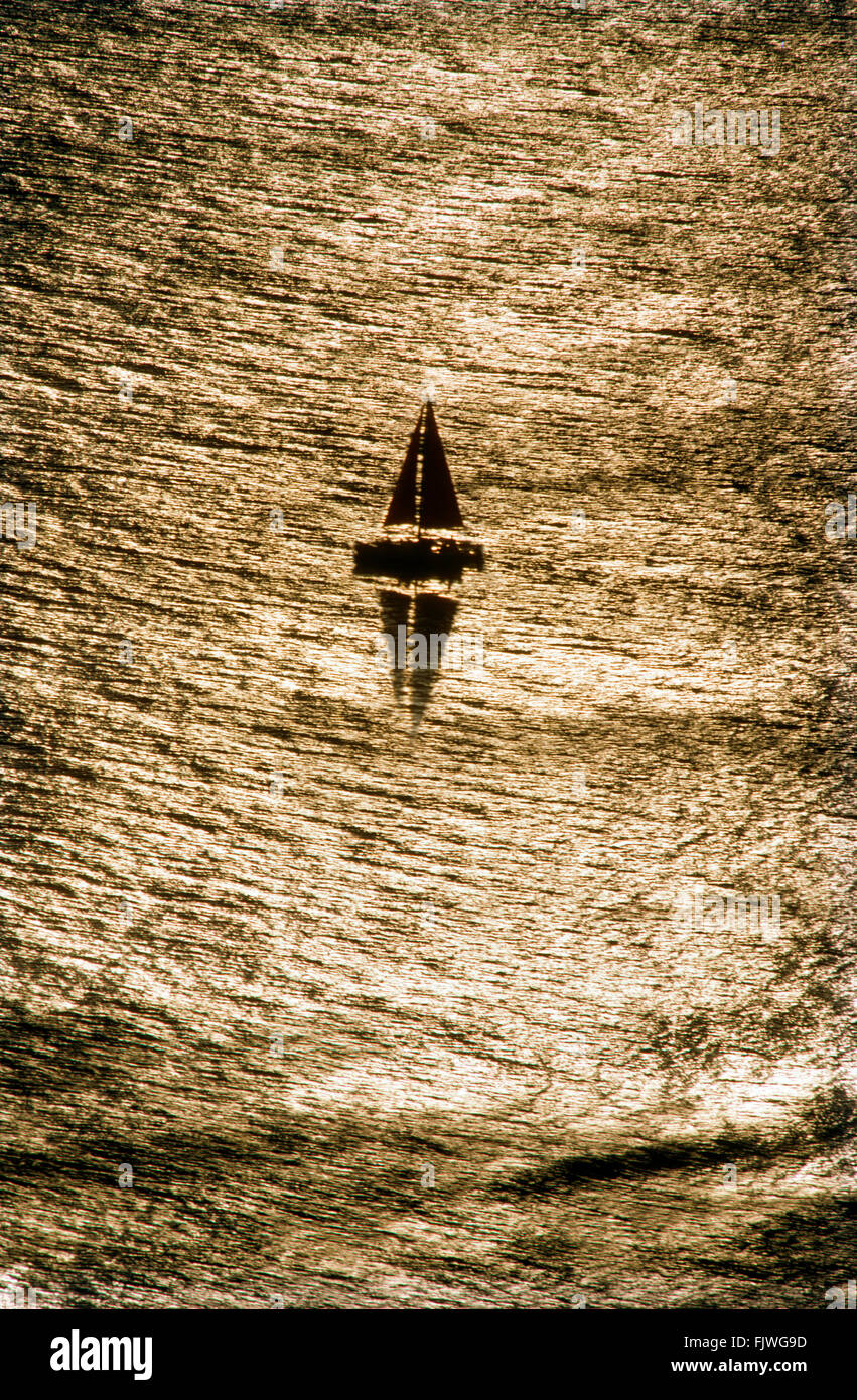 barco de vela Lone en el tranquilo Océano Pacífico frente a la costa de California con el sol se refleja a través de la superficie de desmotado Foto de stock
