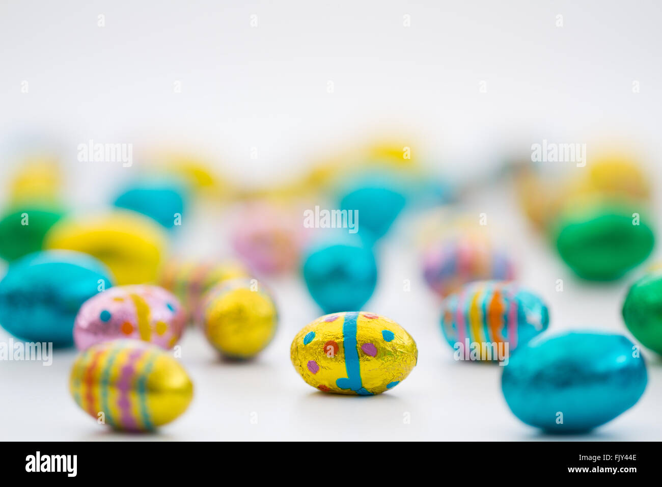 Montones de pequeños, coloridos huevos de pascua esparcidos sobre un fondo blanco. Foto de stock