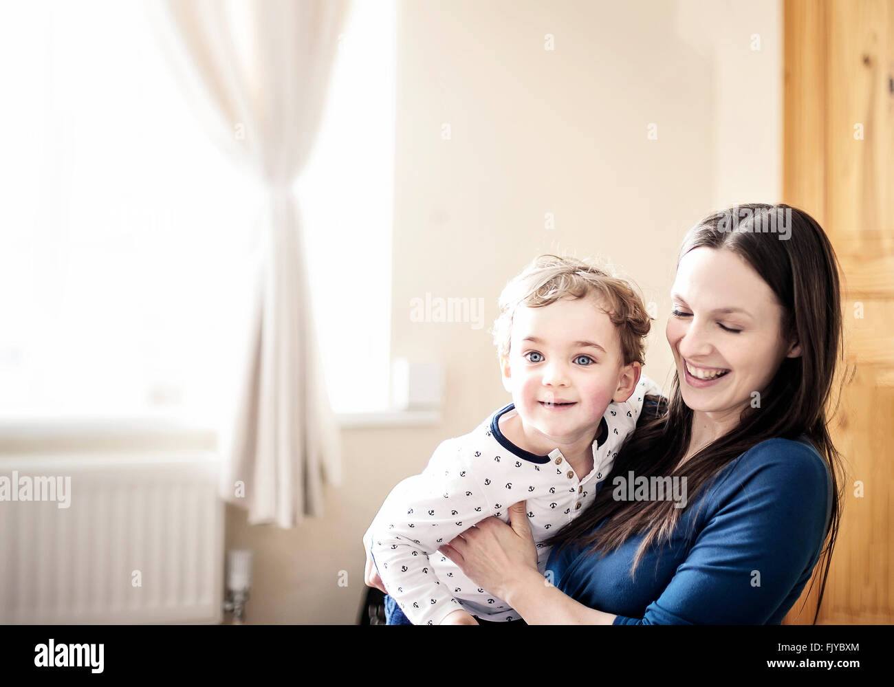 Mamá joven jugando con su niño pequeño en la habitación Foto de stock
