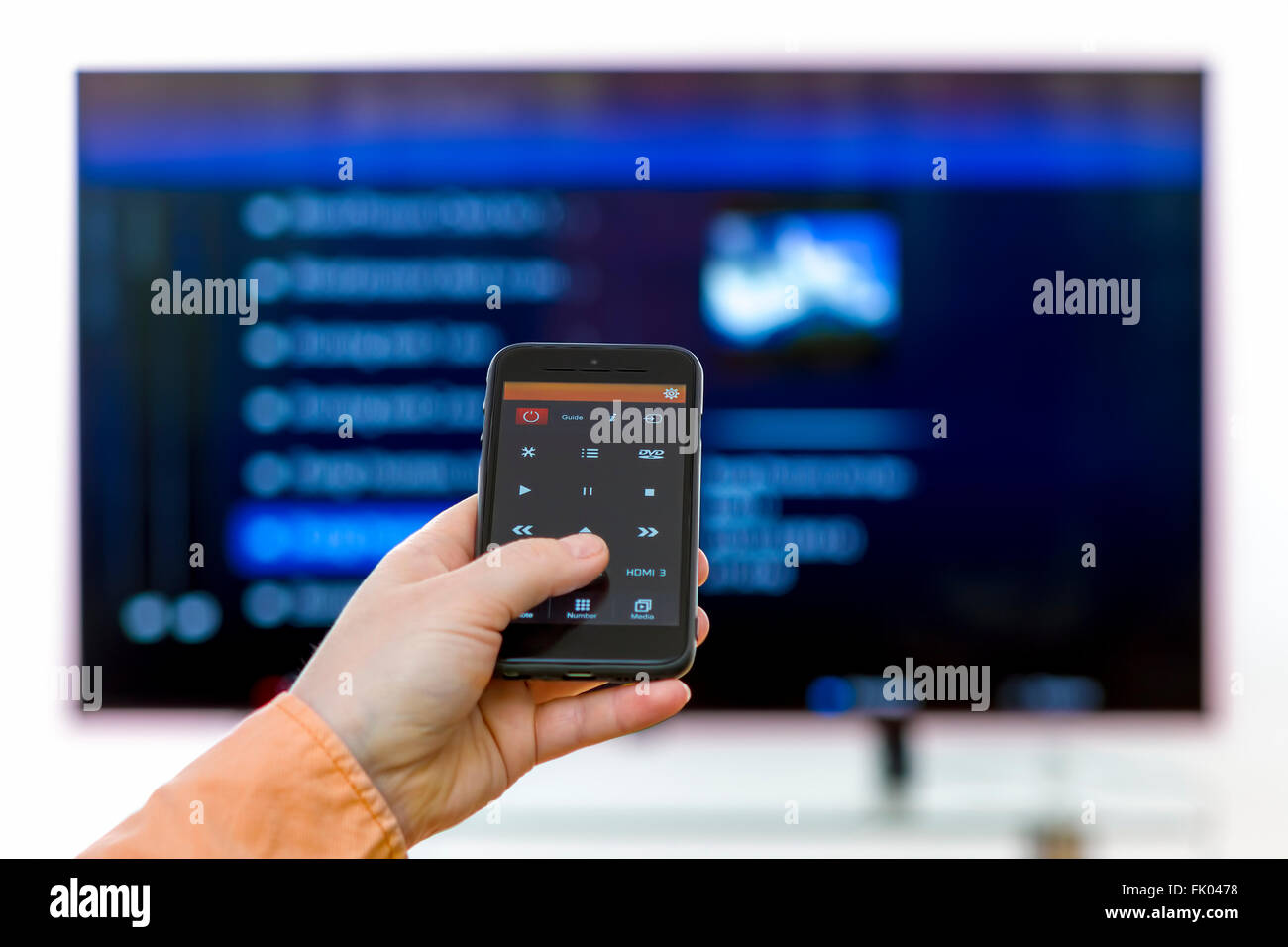 Primer plano sobre la mujer mano sujetando el smartphone y utilizar una app con control remoto y programas de navegación en la televisión. Foto de stock