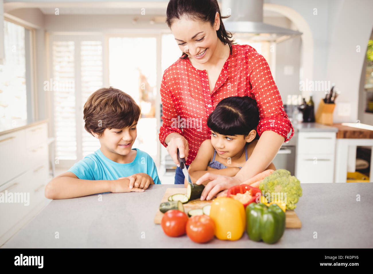 Mujer picar las verduras mientras los niños de pie en la tabla Foto de stock