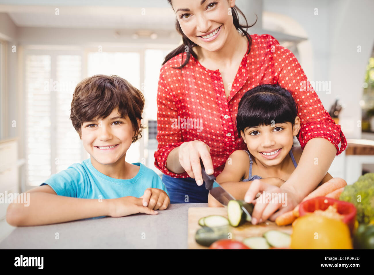 Feliz mujer con hijos picar las verduras en casa Foto de stock