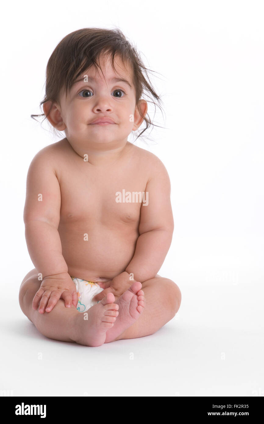 Bebé niña está sentada en el suelo con una extraña expresión sobre fondo blanco. Foto de stock