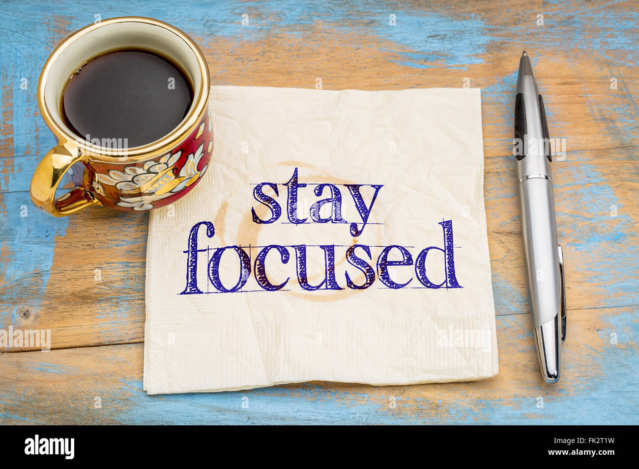 Manténgase enfocado recordatorio o asesoramiento - escritura en una servilleta con una taza de café contra una madera pintada grunge Foto de stock