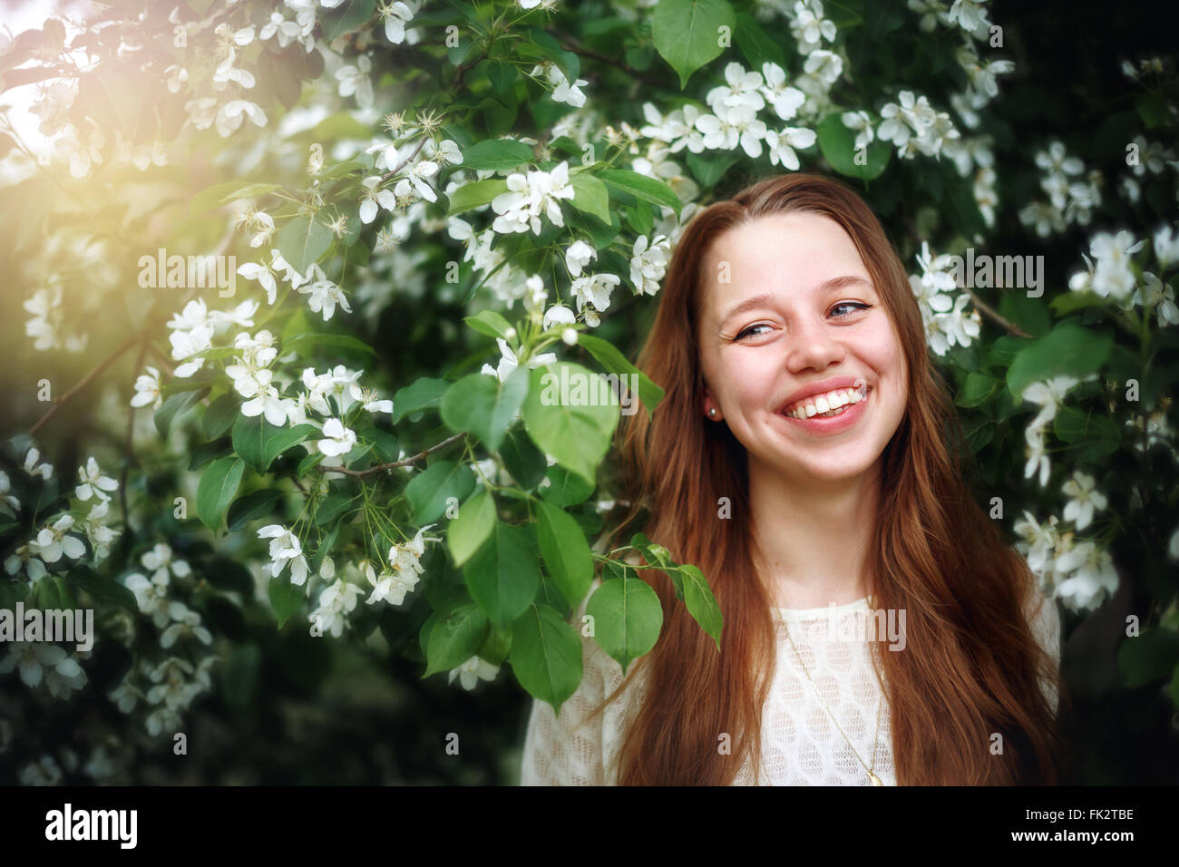 Headshot retrato de joven bella entre las flores de la primavera en la naturaleza. Mujeres riendo y disfrutando de la vida y del momento. Foto de stock