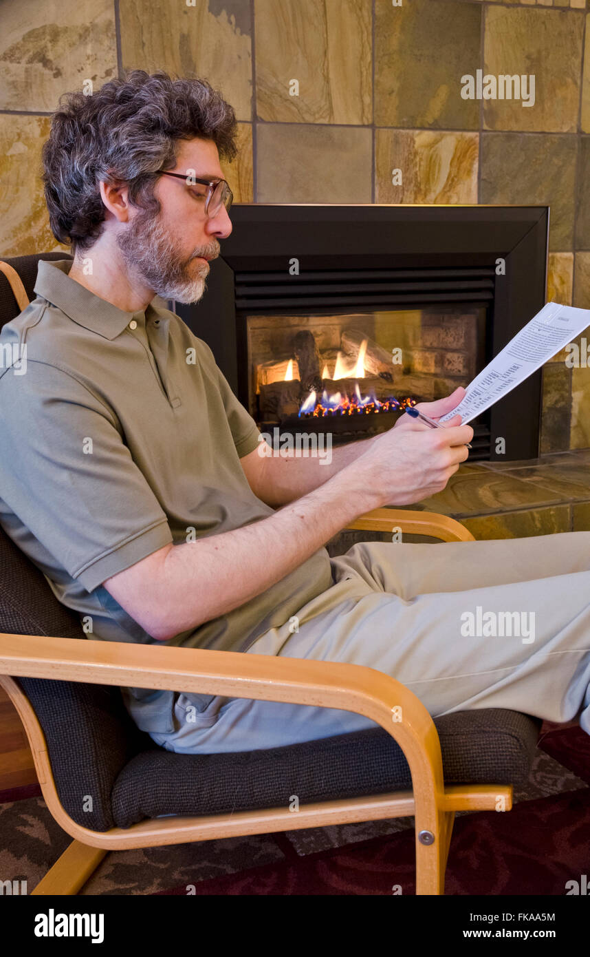 Distinguidos hombres caucásicos de mediana edad sentado cerca de una chimenea de lectura académica o un informe financiero. Foto de stock
