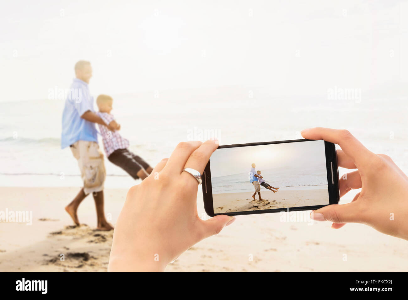 Perspectiva Personal de mujer fotografiando padre jugando con su hijo (12-13) en la playa Foto de stock