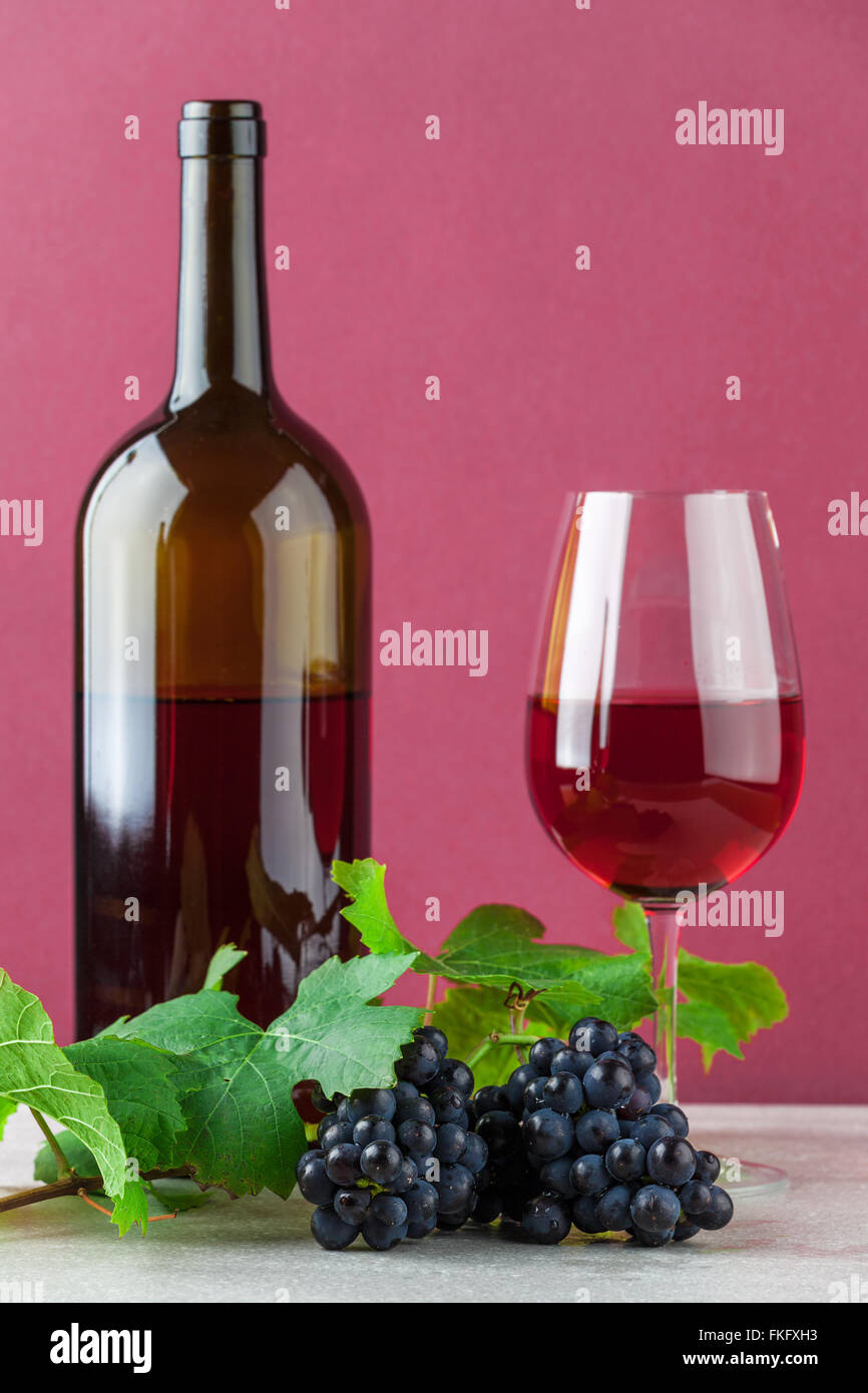 Botella de vino tinto y wineglass con uvas maduras en mármol y color rosa de fondo Foto de stock