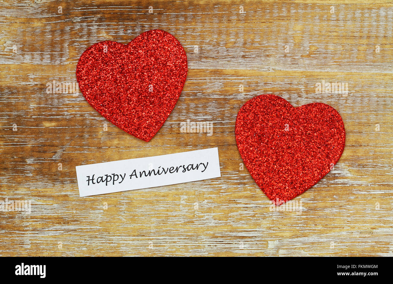 Feliz Aniversario tarjeta con dos corazones rojos brillantes sobre la superficie de madera rústica Foto de stock