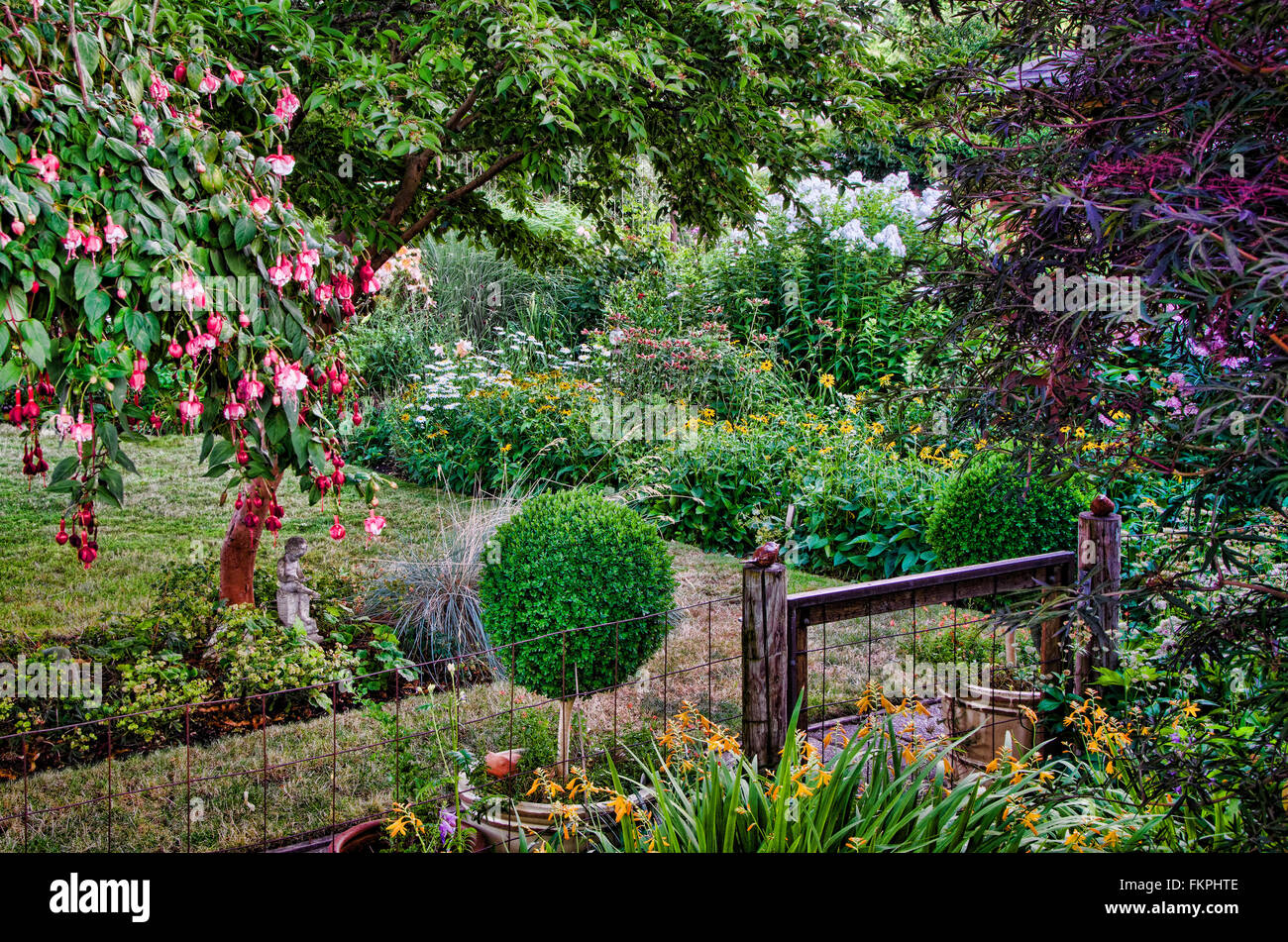 Un rústico portón flanqueado por dos mesas hedge arbustos conduce a un país tranquilo jardín hecho en un nostálgico estilo ilustrativo. Foto de stock