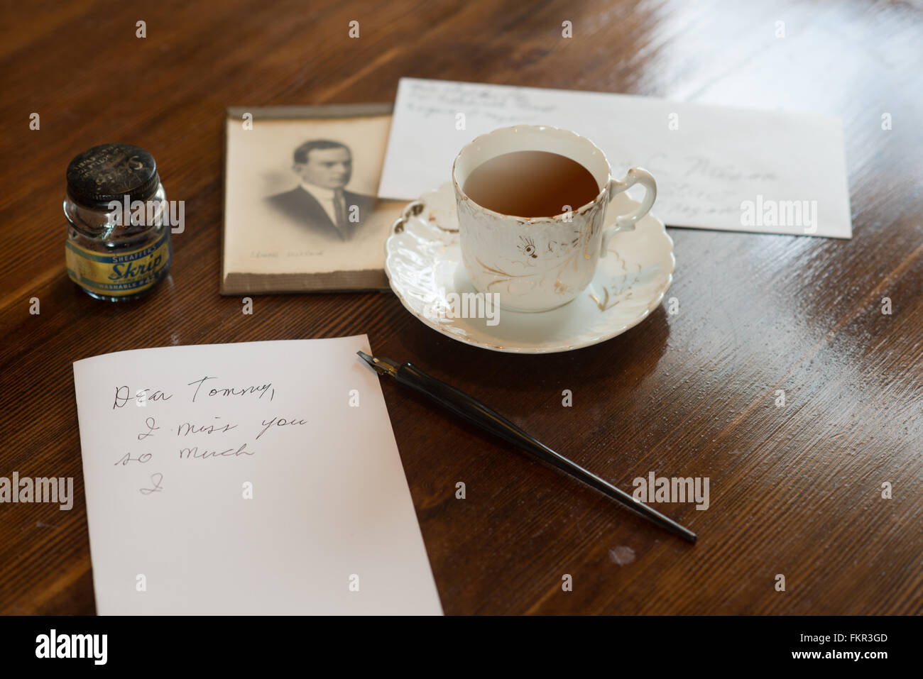 Todavía la vida de antaño de una carta escrita parcialmente en una vieja mesa con té y una fotografía sepia en el fondo. Foto de stock