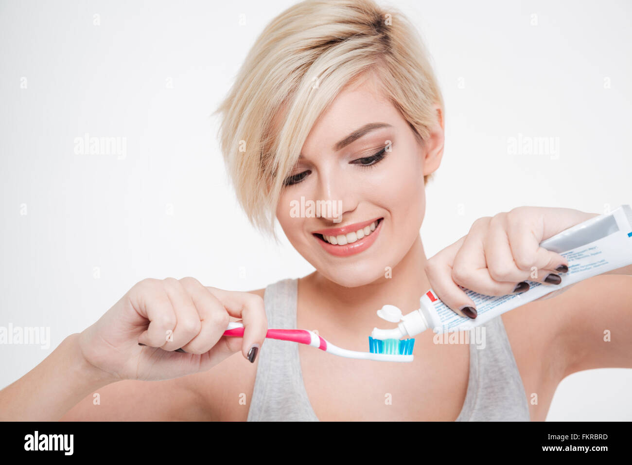 Mujer sonriente sosteniendo un cepillo de dientes y dentífrico poniendo aislado sobre fondo hite aw Foto de stock