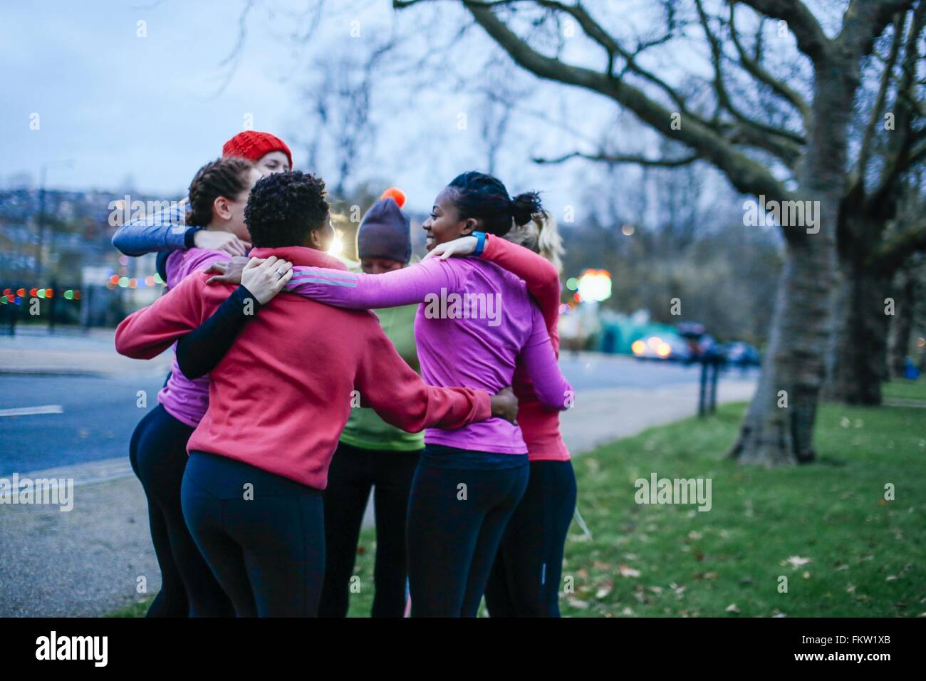 Seis corredores femenina adulta compartiendo la motivación se apiñan en el borde de la ciudad al atardecer Foto de stock