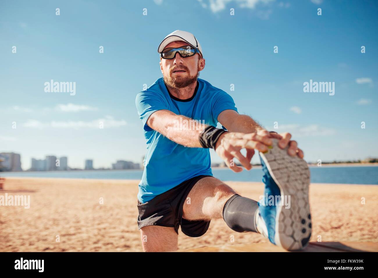Mitad hombre adulto en la playa de la pierna levantada de tocar los dedos del pie estiramiento, Dubai, Emiratos Árabes Unidos. Foto de stock